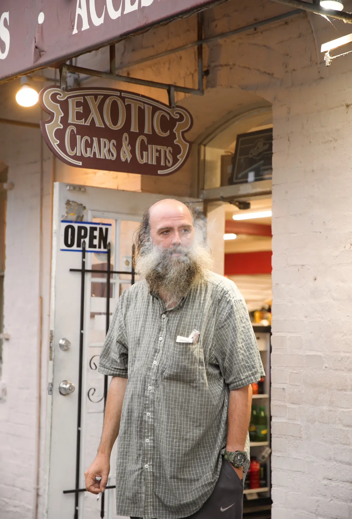 A bearded man standing in the doorway of a cigar and gift shop.