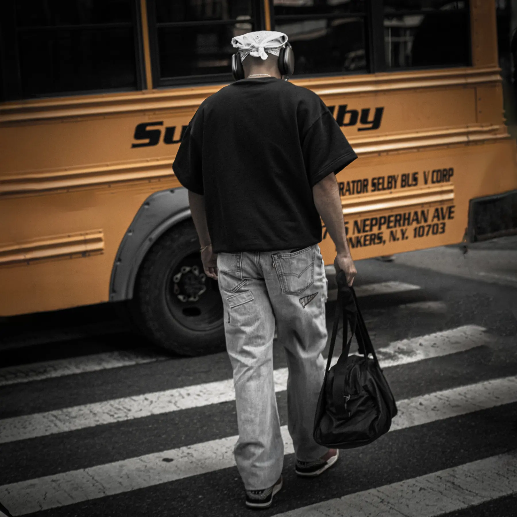 A man walking across a crosswalk past a yellow school bus, seen from behind.