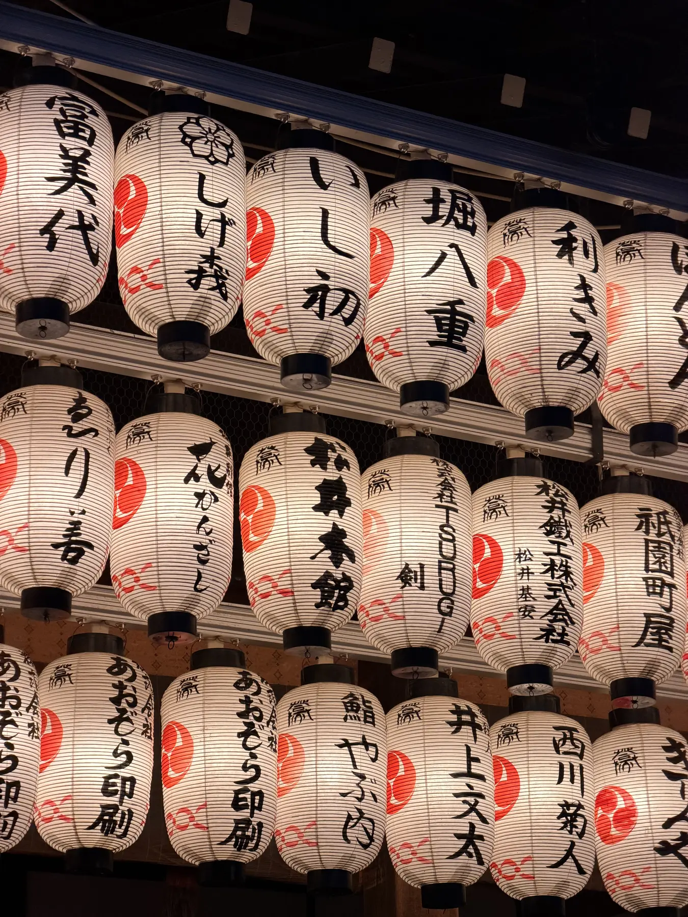 A wall of lit paper lanterns, each with a donor's name in black brushwork.