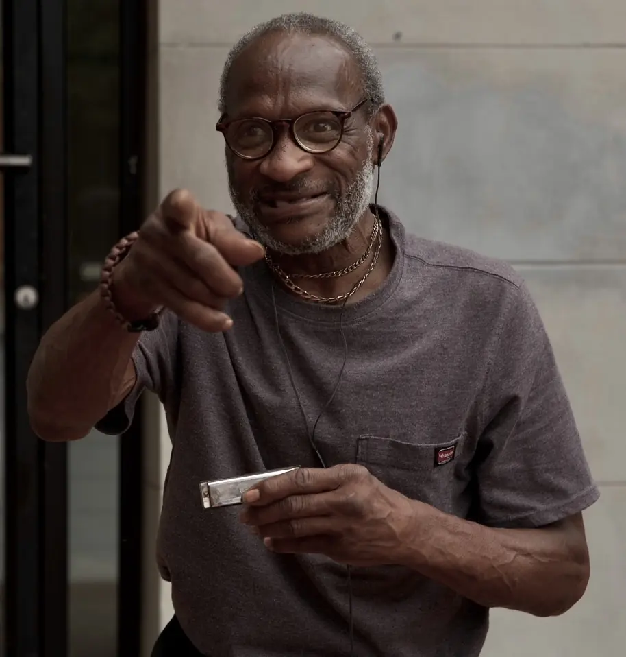 An older man in glasses laughing and pointing at the camera.