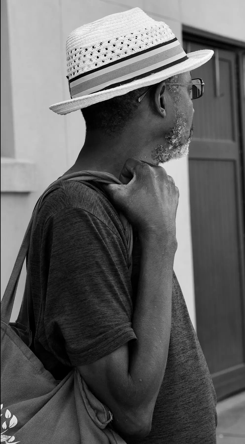 Black and white profile of the man in the straw hat, looking away, a bag over his shoulder.
