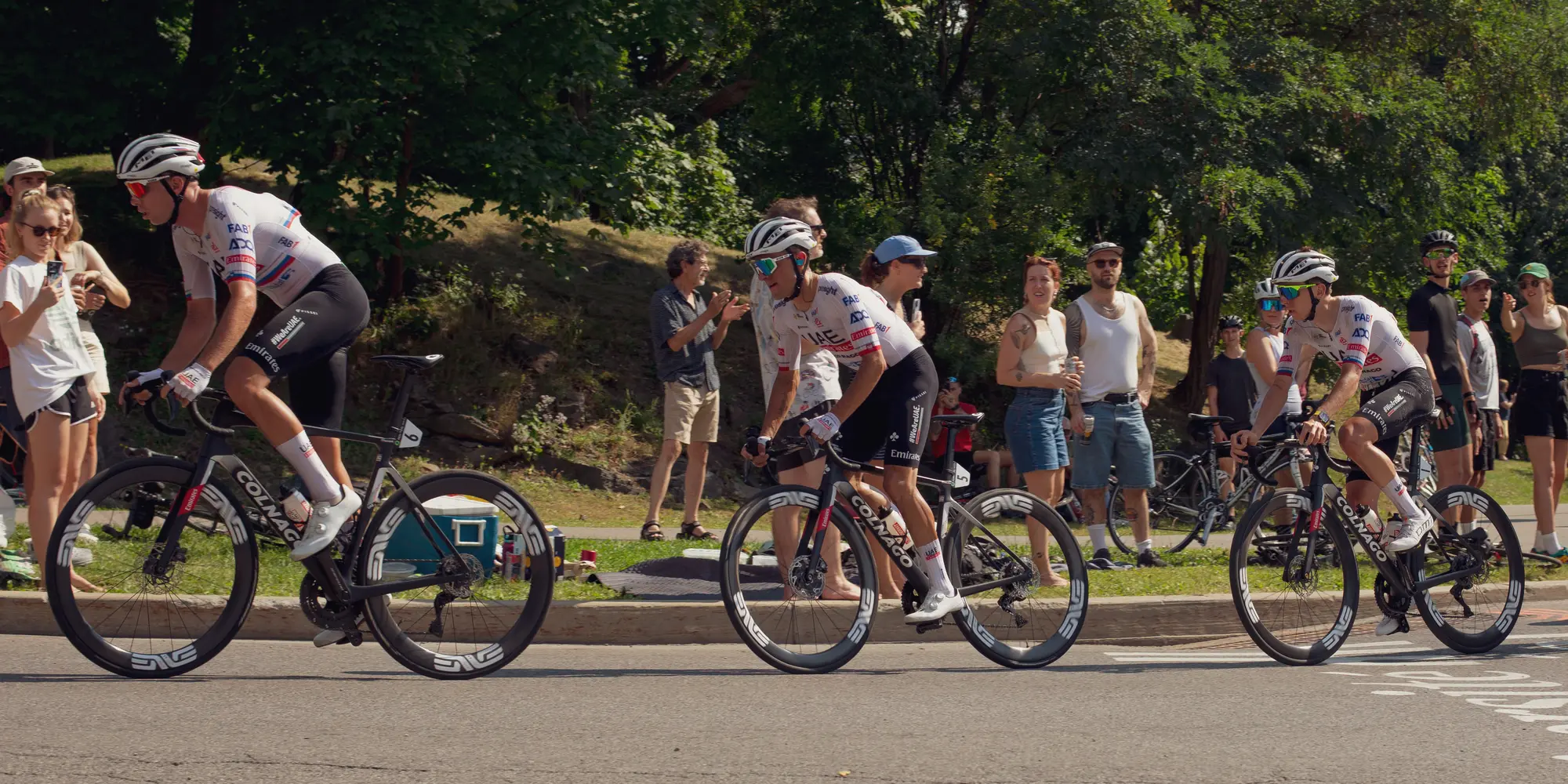 Three riders strung out along a curve past spectators on a grass bank.