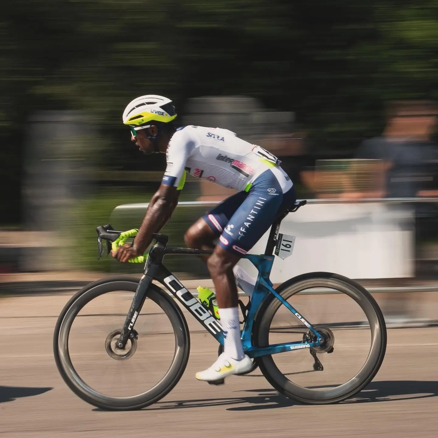 Two riders side by side at speed, one in a pink kit behind one in white.