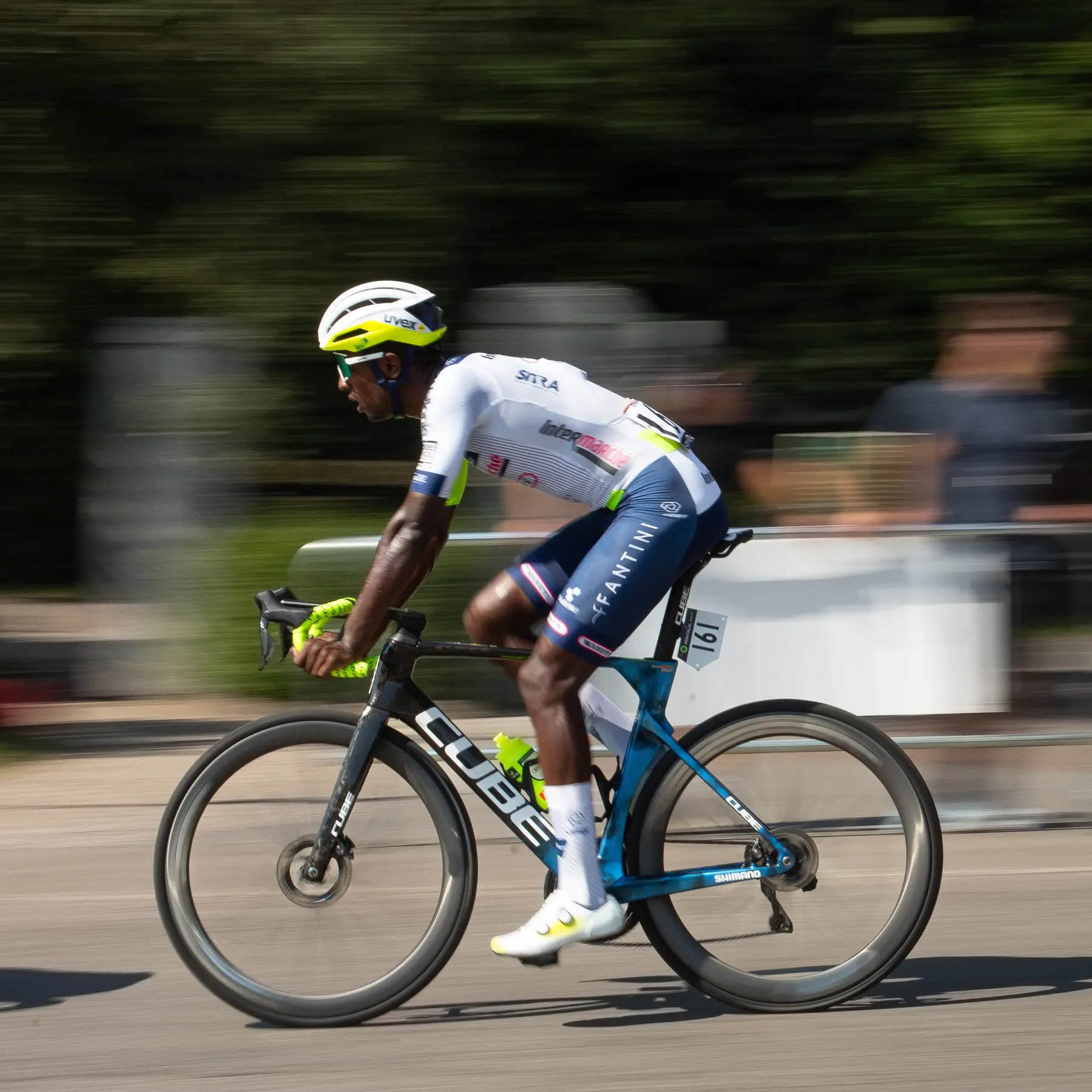 A rider in a white team kit sprinting past on a black and blue bike, the background streaked by a panning shot.