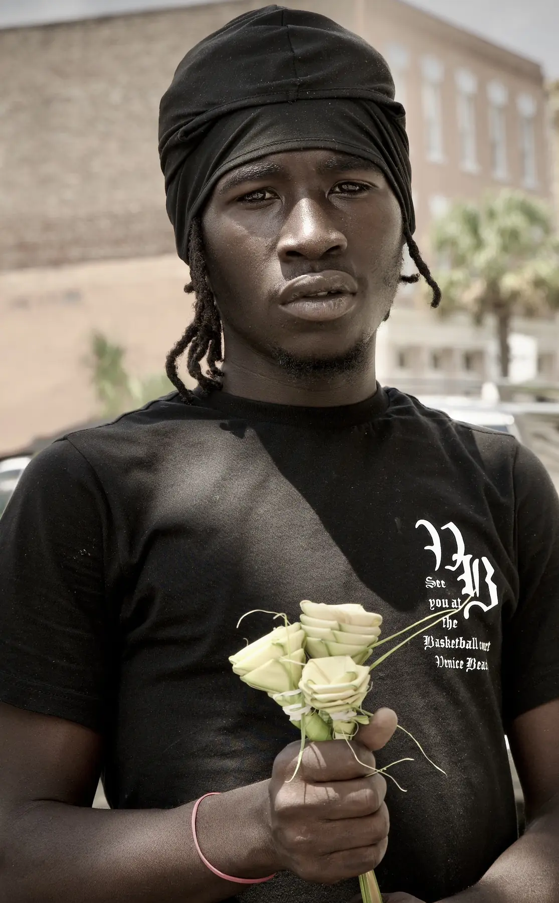 A young man in a black head wrap holding a small bunch of white roses.